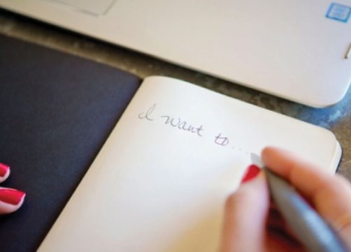 Woman writing I want to on notebook